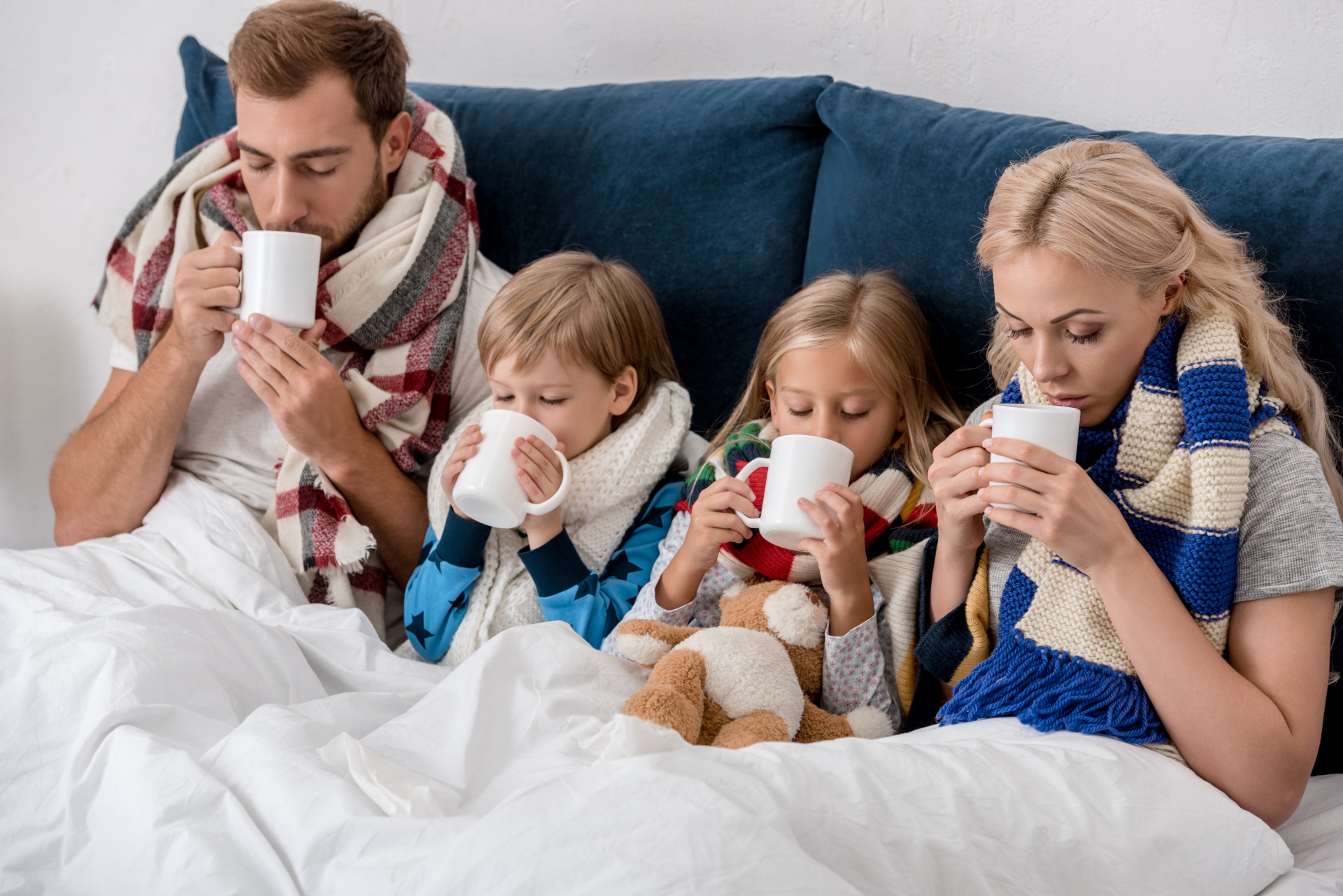 sick young family drinking warming beverages while sitting in bed