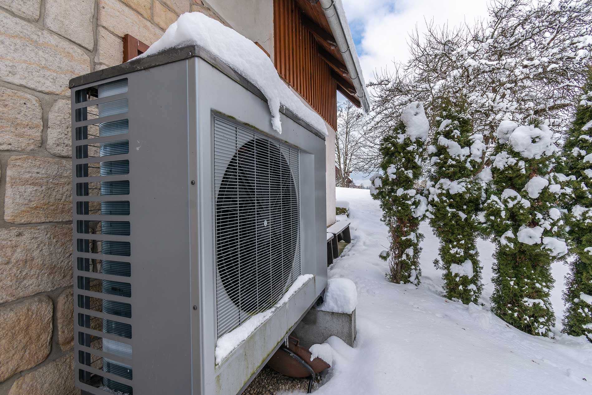 Air-heat-pump-covered-with-snow-beside-house-in-winter